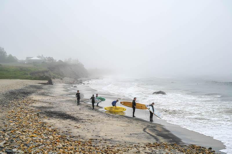 Several men in wet suits with surfboards on a rocky Martha's Vineyard beach
